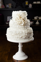 Three tier cake encased in layers of ruffles and accented with an antique white gumpaste rose. A tribute to Maggie A.